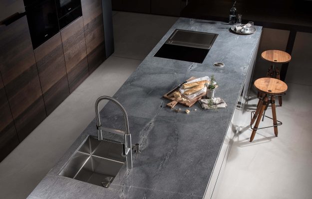 Elegante Kücheninsel mit grauer Natursteinplatte, integriertem Spülbecken, Kochfeld und hochwertigen Holz-Details – modernes Küchendesign.