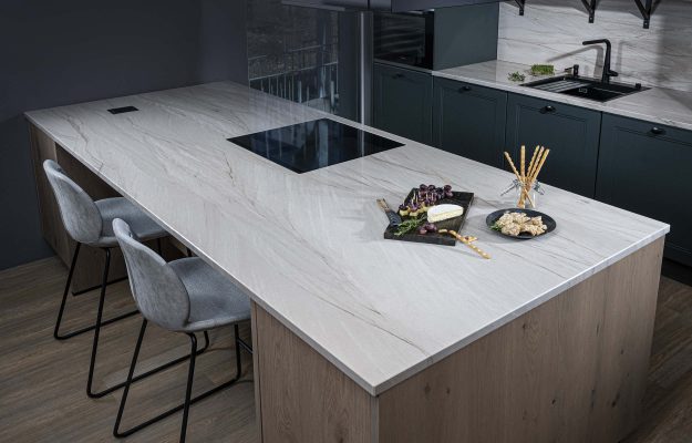 Großzügige Kochinsel mit heller Naturstein-Arbeitsplatte, modernem Induktionsfeld und stilvoll arrangierten Speisen – luxuriöse Küchengestaltung.