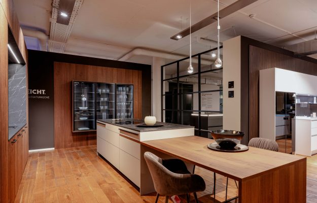 Luxuriöse Ausstellungsküche mit kombinierter Holz-Esstischlösung, heller Insel, dunkler Glasvitrine und modernen Designleuchten – exklusives Küchenambiente.