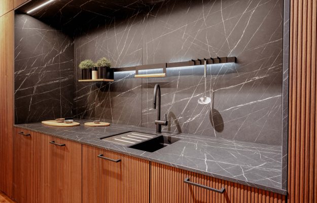 Exklusive Küchenzeile mit schwarzer Marmor-Arbeitsplatte, schwarzer Designarmatur und vertikalen Holzfronten – edle Materialkombination im modernen Küchenbau.