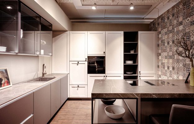 Exklusive Landhaus-Designküche in Weiß und Grau mit modernem Küchenblock und strukturierter Fliesenwand im Showroom Göttingen.