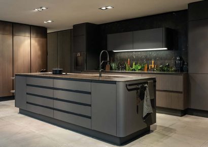 Moderne Premiumküche in dunklem Holz und Grau mit großer, gerundeter Kochinsel und beleuchteter Rückwand – elegantes High-End-Design.