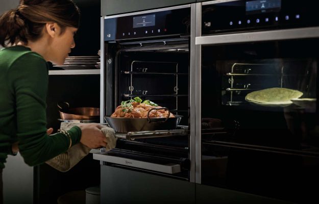 Neff Einbau-Backofen: Moderne Szene mit Neff Einbaubackofen, in den eine Frau gerade ein Gericht einschiebt