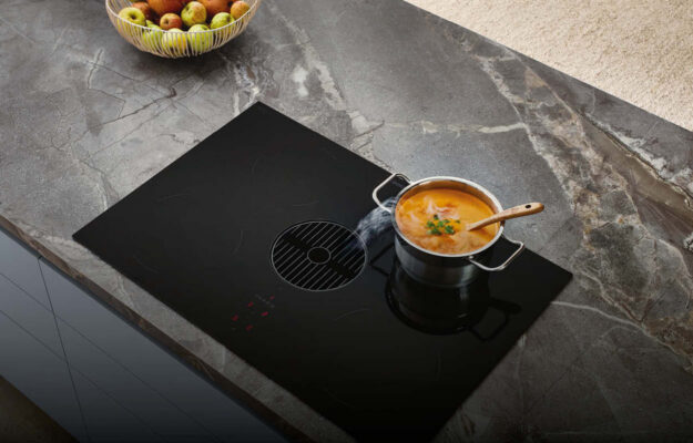 Arbeitsplatte von Nobilia mit integriertemKochfeld und Dunstabzug in schwarzem Glas, kochtopf mit Suppe, für effizientes Kochen und Absaugen von Dampf